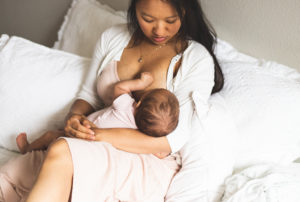 Mom breastfeeding baby on bed in pink dress. 