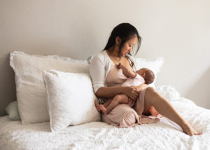 Mom breastfeeding baby in a pink dress in the primary bedroom on bed. 