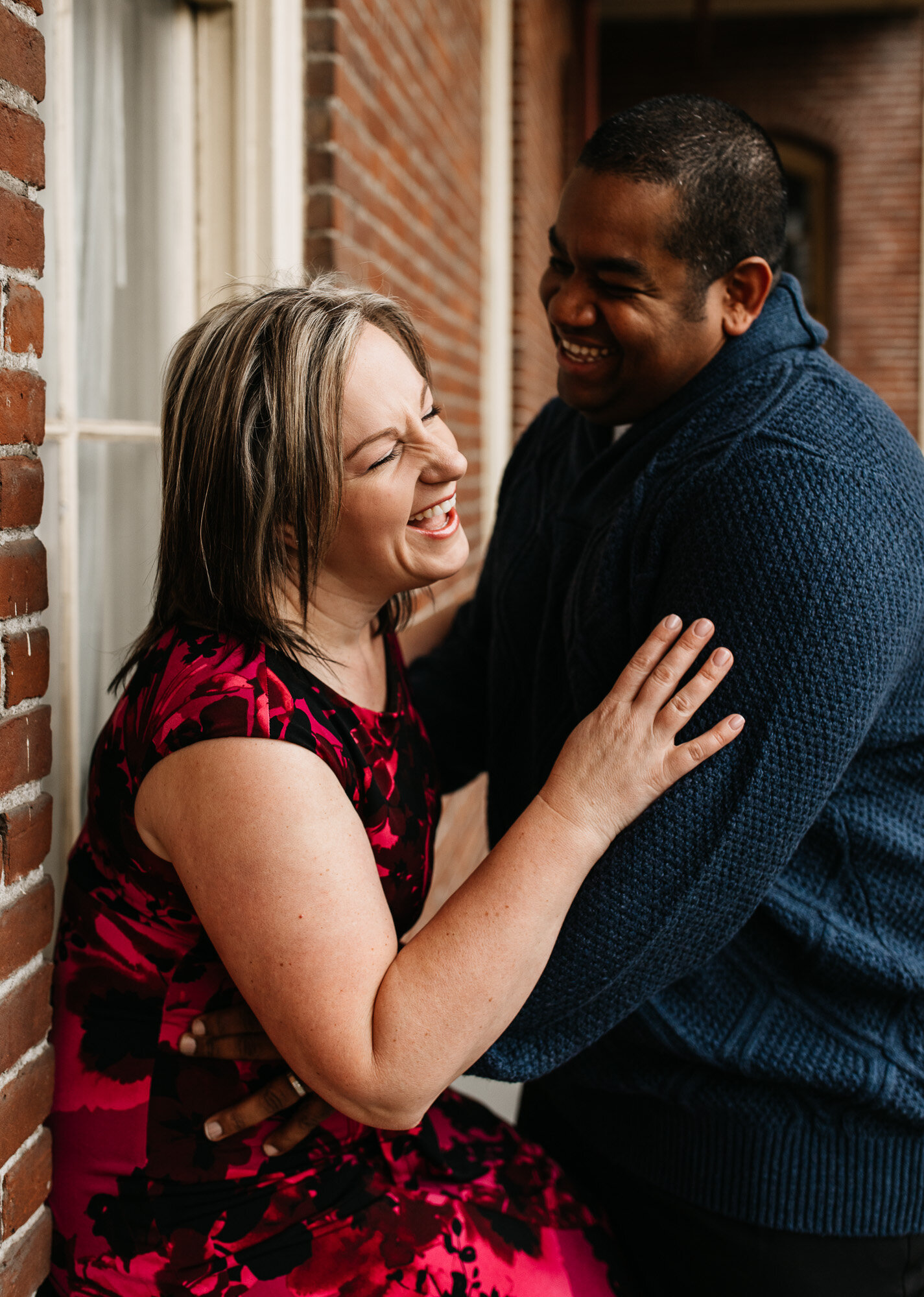 The best time of year for outdoor portrait photography | husband and wife laugh against a brick wall at a historic church near Portland, Oregon.