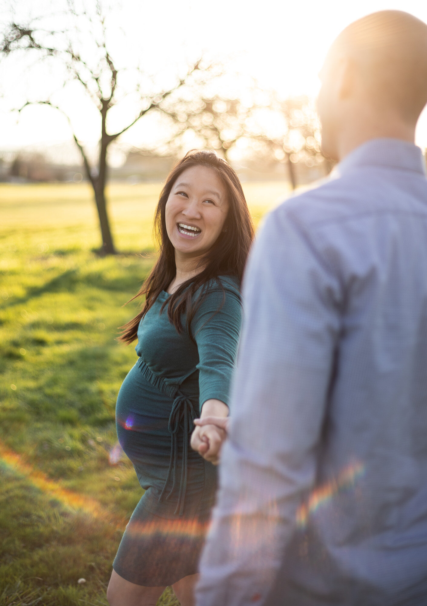 Maternity photography Vancouver Washington | Pregnant woman smiling at her husband at they walk towards the sun holding hands. 