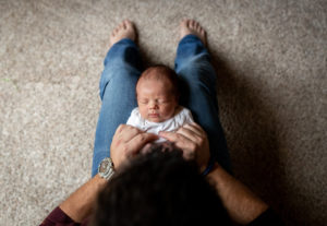 Dad holding newborn in lap on floor. 