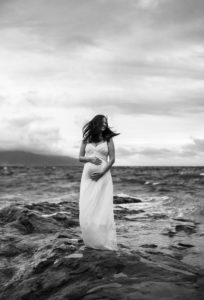 Rainy Portland area maternity photo shoot. Black and white image of mom-to-be on the rocks at Cape Kiwanda beach