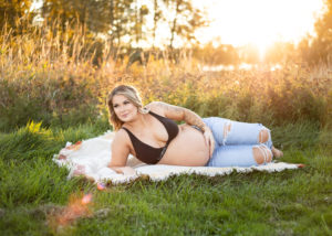 pregnant woman holding belly laying in grass in field. 