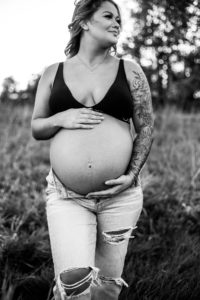 black and white image of expectant mother touching her belly in feild near Portland Oregon 