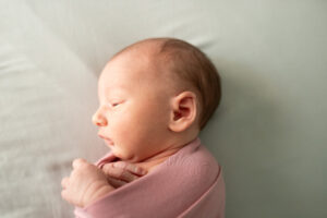Baby laying on her side in light pink swaddle. 