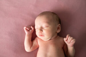 Newborn sleeping on soft pink blanket in a blog for what to wear for newborn photos. 