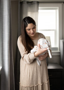 Mom doting on newborn son naturally lit by window in blog about what to wear for newborn photos. 