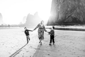 Black and white image of a mom with sons walking in front of haystack rock. Pacific City Hotels Oregon