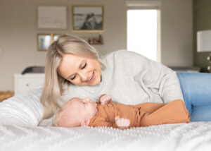 Mom laying next to her newborn baby, wearing a burnt soft orange swaddle. The blog covers what to wear for newborn photos. 