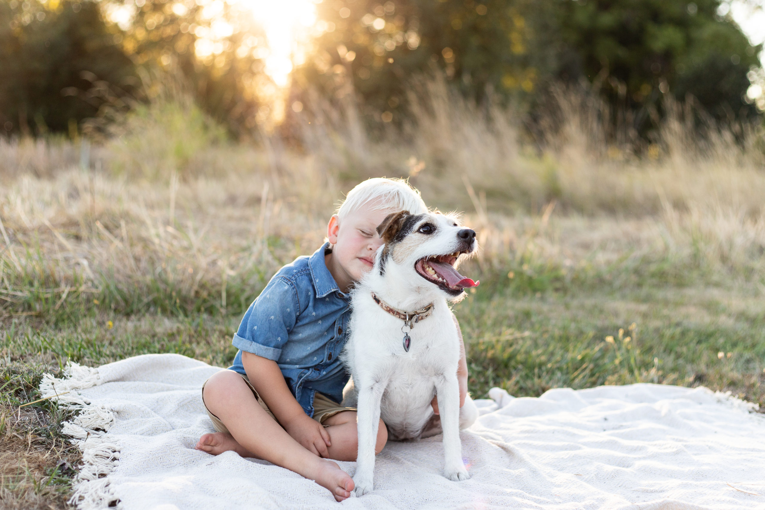 A boy and his dog sitting on blanket in a field. 