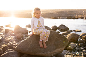 A young girl sitting on rock at Lincoln City at sunset. 