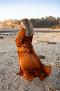 Mom standing on beach at sunset in rust colored max dress. 