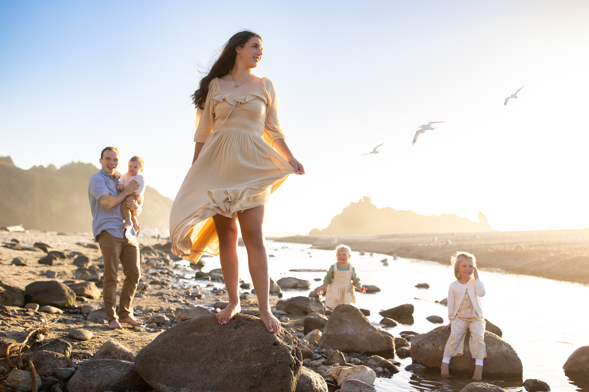 Oregon Coast photographer captures mom standing on rock with family behind her at sunset on the beach.