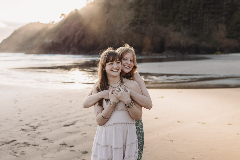 Two sisters smiling together on the beach during golden hour during an oregon coast photography session.