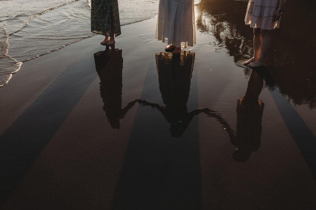 Reflection of a couple holding hands in the wet sand at sunset.