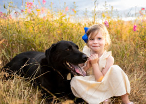 Little girl with black lab sitting in flower field. 