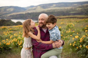 Exploring the Columbia River Gorge Scenic Area with Kids. Dad hugging two young kids in a yellow wildflower field. 