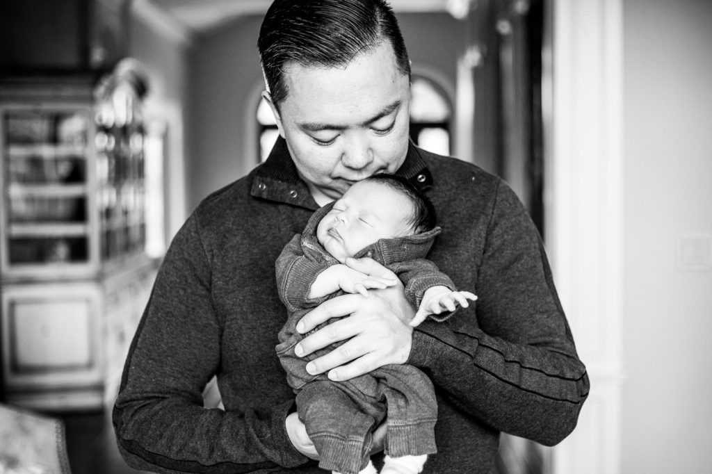 Black and white image of Dad holding newborn baby in living room