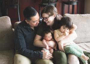 Family of four sitting on the couch hugging in their newborn photo shoot near portland, Oregon. Portland baby stores. 