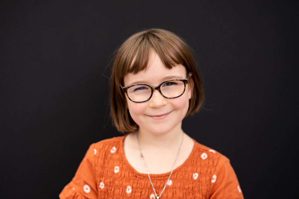 Vancouver Washington Private Schools | School portrait of a little girl with glasses against a black backdrop. 