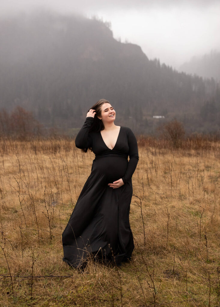 Pregnant woman holding her belly in the Columbia River gorge, wearing a black dress | Maternity dresses for photoshoot 