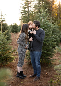 Pregnant mom kissing daughter and husband at tree farm in PNW.