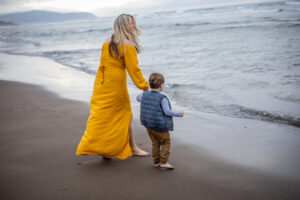 Mom in yellow dress holding sons hand walking into the shore at Cape Kiwanda, Oregon. 