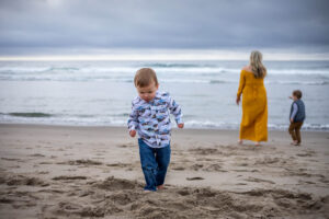 Things to do in Pacific City, Oregon for families. Mom in a yellow dress and two little boys are playing on the beach at Cape Kiwanda. 