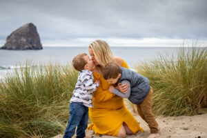 Mom of two little boys sitting on the beach in Pacific City, Oregon wearing a yellow dress. 