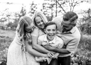 Black and white image of a family in Hood River, Oregon hugging youngest sibling. 