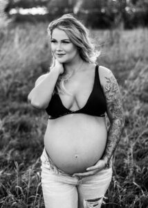 black and white image of pregnant woman in field wearing Calvin Klein bra and jeans