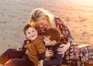Family of three sitting on the sand at Cannon Beach, Oregon, at sunset.