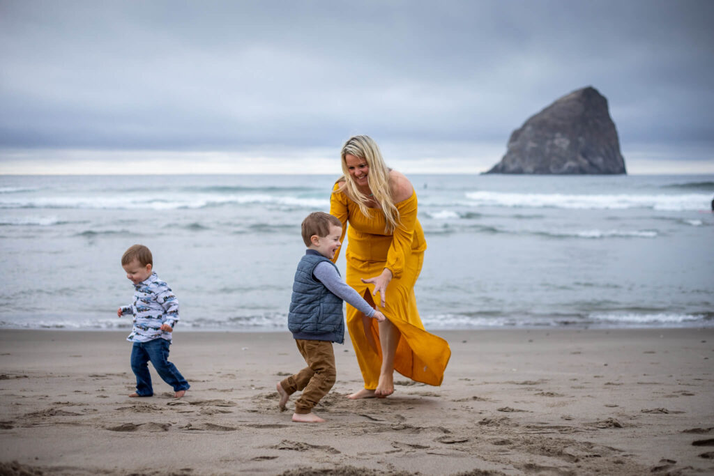 Mom in a yellow dress chasing two little boys in front of Haystack Rock in Pacific City, Oregon. 