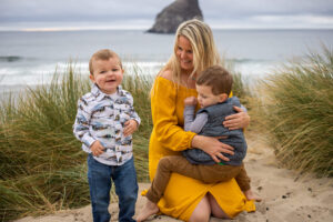 Mom in a yellow dress sitting on the beach with two little boys in Pacific City, Oregon. 