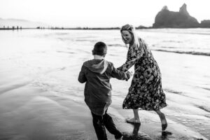 Black and white image of mom and her son running on the beach at Cannon Beach, Oregon. Things to do in the Oregon coast. 