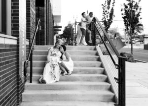 Black and white image of mom and daughter sitting on steps and dad with son standing by apartments in front of Washington Street in Vancouver Washington