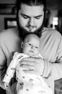 Black and white image of new dad holding newborn son. 