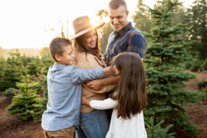 Family of four hugging in a PNW tree farm for holiday photos at sunset. 