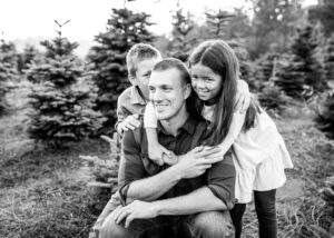 Black and white image of dad with two kids hugging at PNW tree farm for holiday photos. Portland Photographer mini session. 