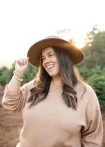 Woman holding fedora hat at sunset smiling near Portland, Oregon. Portland Hair Salons