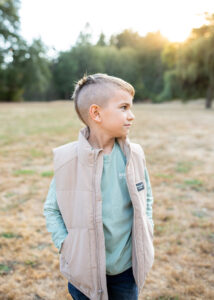 Young boy with modern hair cut looking off at his parents in beautiful park in the PNW. 