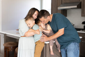 Family of four embracing in their kitchen for an in-home family photo shoot. 
