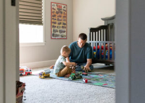Dad and son playing with toys in boys room. 