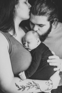Black and white image of a newborn in mother's arms with dad kissing newborn's head. Portland pediatricains. 