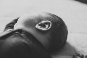Black and white image of newborn babys ear while he is sleeping on a bed. 
