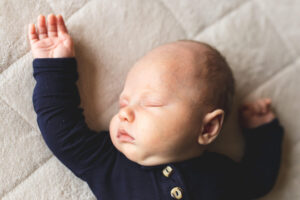 Newborn baby sleeping peacefully on the bed with right arm up. 