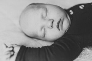 Black and white image of newborn baby sleeping on the bed. Portland baby photographer