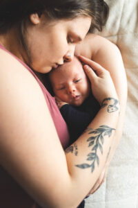 New mother and newborn son embracing while laying on a bed. 