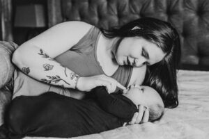 Black and white image of mom and newborn baby laying on the bed. Mom is doting over newborn son's lips. 