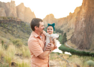 A Dad holding infant daughter at sunset in Smith Rock State Park. Things to do in Bend, Oregon with kids. 